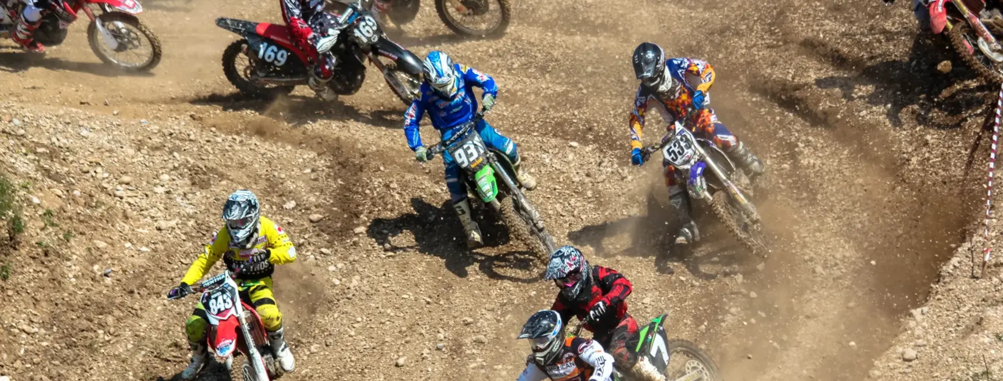 A pack of riders through a rutted berm at a club motocross meeting